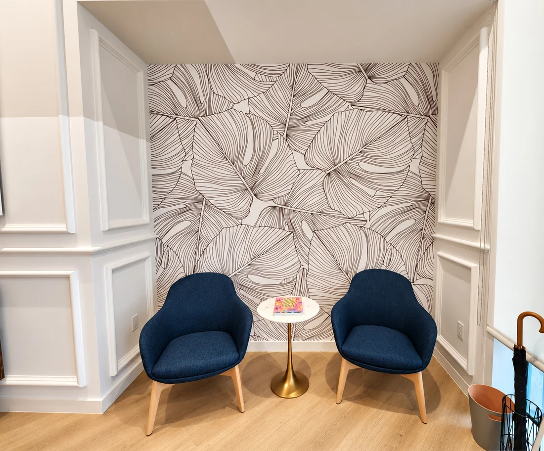 One Medical — Two navy armchairs and a brass side table in front of a wall of oversized line-drawn leaves